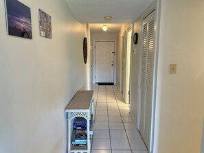A hallway with a door at the end, a small table with board games, and a wall-mounted clock. - Land's End Resort - King Suite w/ Peaceful Views | Perfect for Couples (Myrtle Beach)