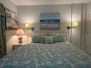 Ein Schlafzimmer mit einem Bett, zwei Wandleuchten, einem Meeresbild und einer Tür.