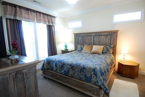 A bedroom with a wooden bed frame, a bedside table, a lamp, and a window with curtains. - Land's End Resort - 2BR House | Gated Resort | Family Friendly (Myrtle Beach)