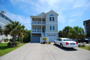 A multi-story residential building with a two-car garage, a balcony on the second floor, and a driveway leading to a white sedan parked in front. - Land's End Resort - 2BR House | Gated Resort | Family Friendly (Myrtle Beach)