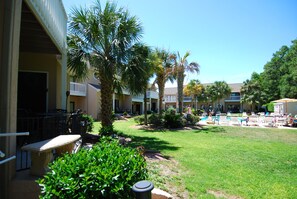 A courtyard with palm trees, a pool area with lounge chairs, and a building with balconies. - Land's End Resort - 3BR Townhouse | Steps to Pool | Nature Views (Myrtle Beach)