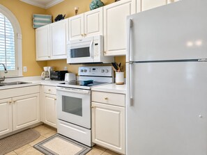 A kitchen with white cabinets, a microwave, a stove, a refrigerator, and a window with blinds. - Land's End Resort - Secluded 2BR Condo | Relaxing Getaway (Myrtle Beach)