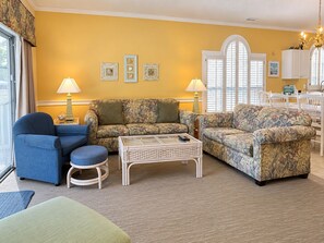 A living room with a sofa set, a blue armchair, a coffee table, and a dining area with a table and chairs. - Land's End Resort - Secluded 2BR Condo | Relaxing Getaway (Myrtle Beach)
