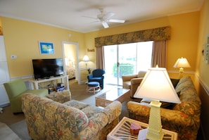 A living room with a television, two sofas, a coffee table, and a ceiling fan. - Land's End Resort - Secluded 2BR Condo | Relaxing Getaway (Myrtle Beach)