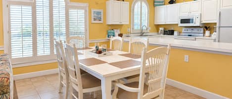 A dining area with a white table and chairs, a chandelier, and a kitchen with white cabinets and appliances.