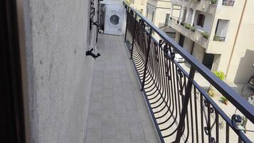 Ein schmaler Balkon mit Metallgeländer, einer Waschmaschine und ein Gebäude mit mehreren Balkonen im Hintergrund.