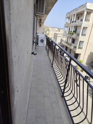 Ein schmaler Balkon mit Metallgeländer, einer Waschmaschine und ein Gebäude mit mehreren Balkonen im Hintergrund.