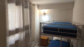 Ein Schlafraum mit Etagenbett, Vorhang, Nachttisch und Wandleuchte.