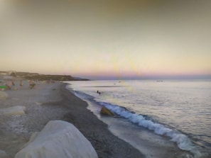 Ein Strand mit ruhiger See, blauem Himmel und ein paar Personen in der Ferne.