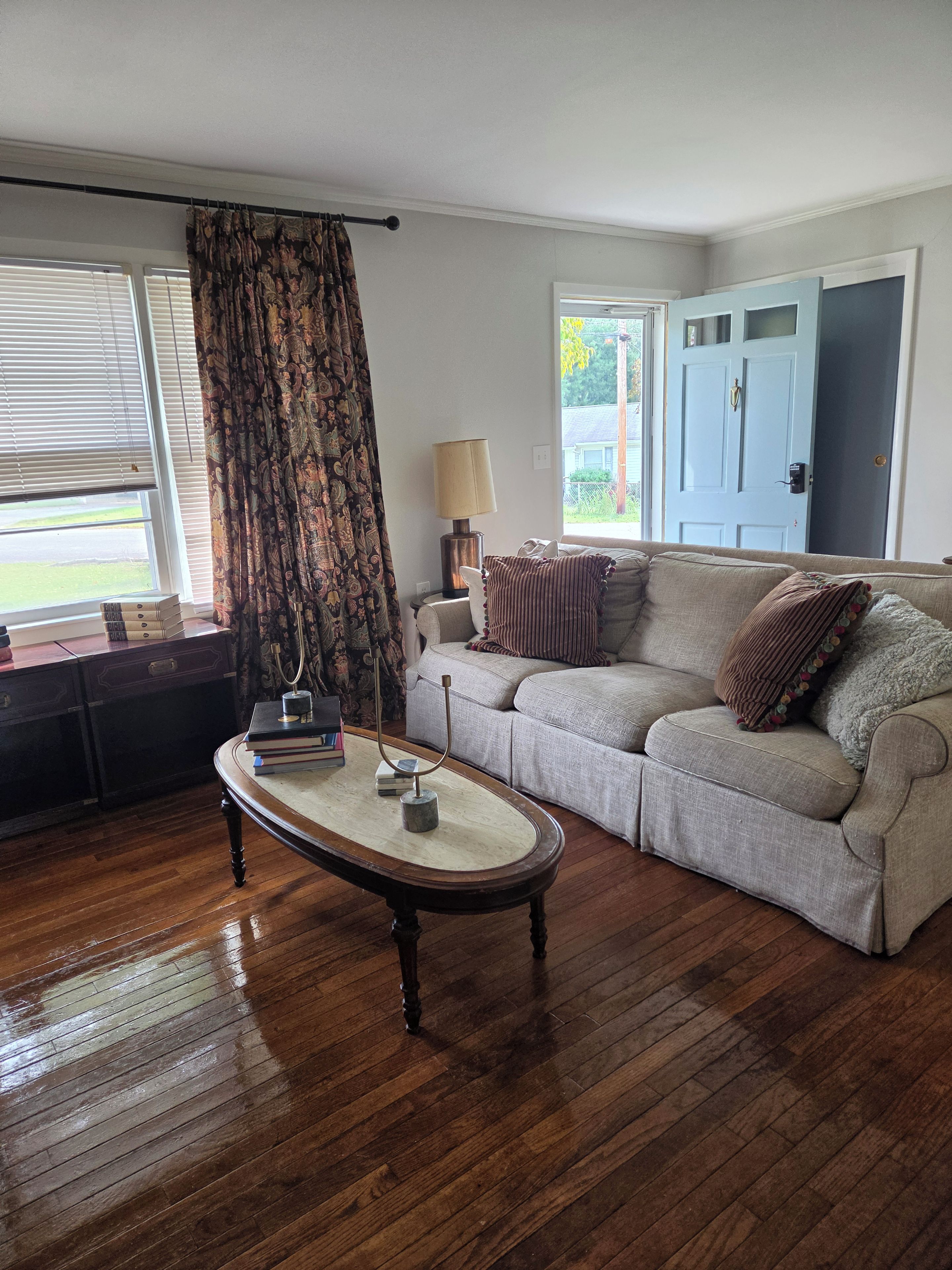 A living room with a wooden floor, a sofa, a coffee table, a lamp, and a door.