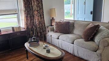 A living room with a wooden floor, a sofa, a coffee table, a lamp, and a door.