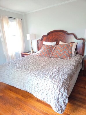 A bedroom with a wooden bed, a patterned throw blanket, and a nightstand with a lamp.