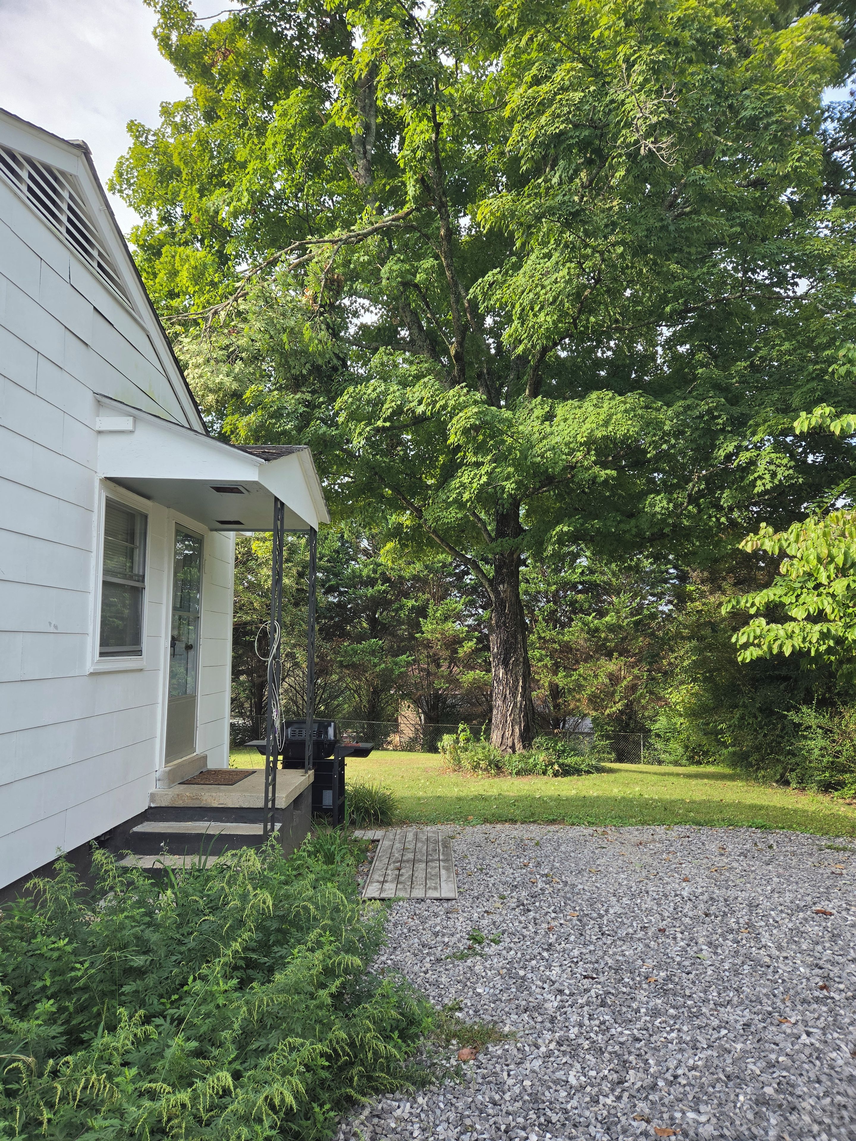 A house with a covered porch, a gravel driveway, and a well-maintained lawn.