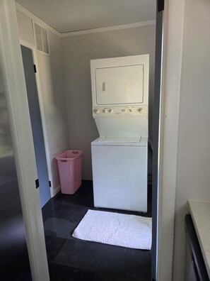 A laundry room with a washing machine, a pink laundry basket, and a white rug on the floor.