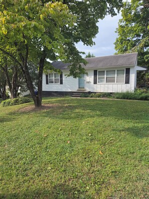 A single-story house with a front porch, a well-maintained lawn, and a tree in the foreground.