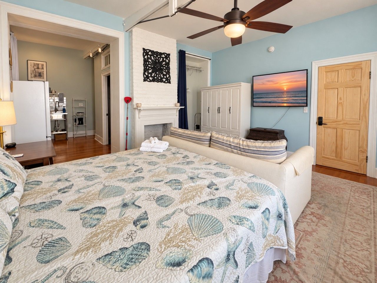 A bedroom with a large bed, a ceiling fan, a fireplace, and a view of the sunset.