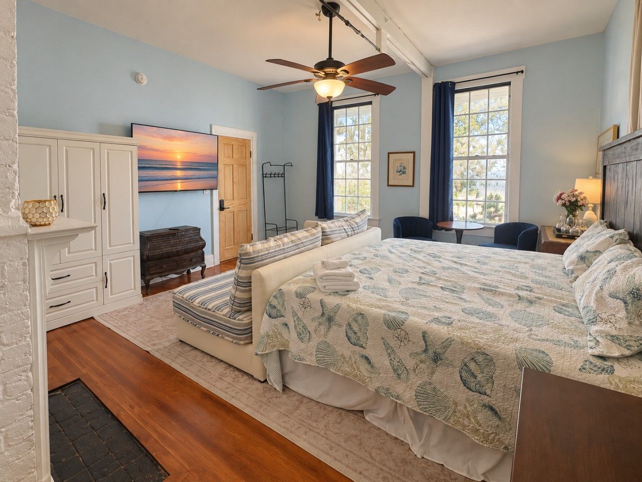 A bedroom with a bed, a ceiling fan, a fireplace, and a window with curtains.