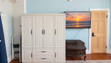 Une pièce avec une armoire blanche, une commode en bois, un téléviseur fixé au mur et une porte.