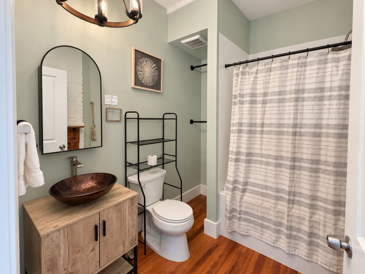 A bathroom with a wooden vanity, a round vessel sink, a toilet, and a shower curtain.