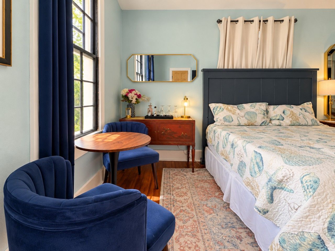 Une chambre à coucher avec un lit, un bureau, une chaise, une table ronde et une fenêtre avec des rideaux.