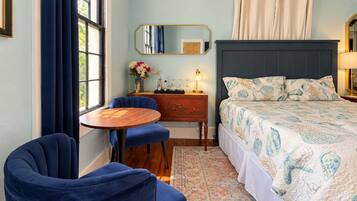 Une chambre à coucher avec un lit, un bureau, une chaise, une table ronde et une fenêtre avec des rideaux.