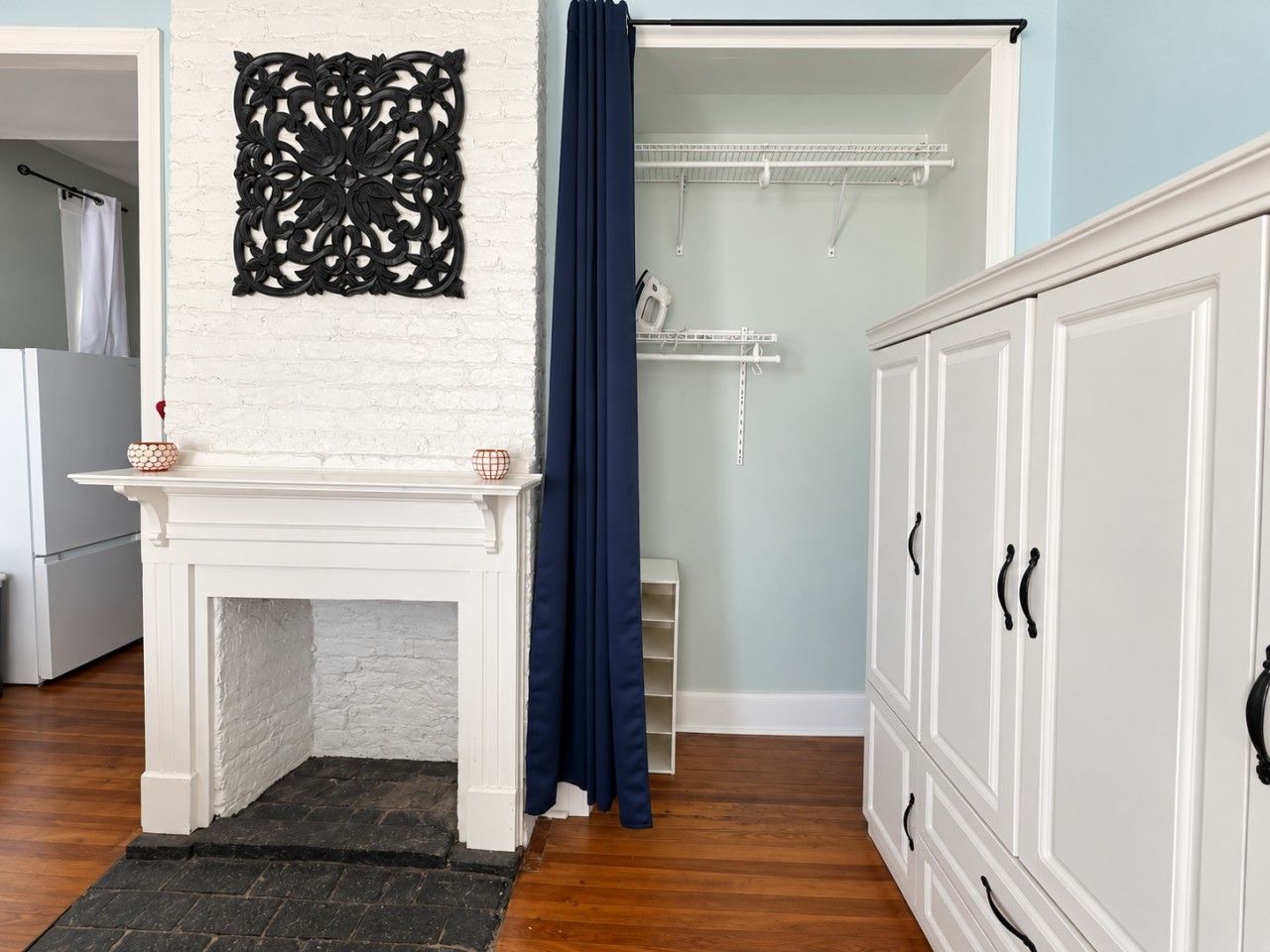 Une pièce avec une cheminée blanche, un élément décoratif mural, un rideau bleu et une armoire blanche.