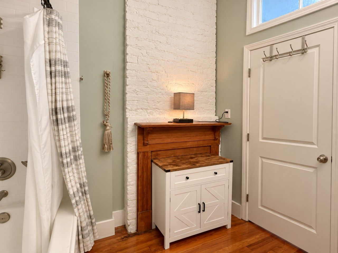 A bathroom with a white door, a wooden cabinet, a towel rack, and a wall-mounted light fixture.