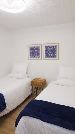 A room with two beds, a small wooden nightstand, and two framed wall art pieces. - "BeeNBee" 3-Bedroom Duplex In the heart of Ybor. (Tampa)