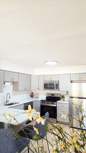 A modern kitchen with grey cabinets, a stainless steel microwave, a stove, and a refrigerator. - "BeeNBee" 3-Bedroom Duplex In the heart of Ybor. (Tampa)