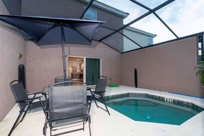 An outdoor swimming pool area with a glass enclosure, two lounge chairs, and a table with an umbrella. - 3BR Bella Vida Townhome Pool & Mickey Room (Kissimmee)