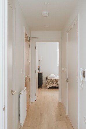 A narrow hallway leading to a bedroom with a bed, a radiator, and a telephone. - Experience London in Luxury – 1-Bed Apt (London)