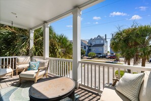 A covered outdoor area with a seating arrangement, including a table and chairs, and a view of a residential street with houses and parked cars. - Private Pool and Hot Tub — 5BR/4BA Beach House with Ocean Views in Surfside Beac (Surfside Beach)