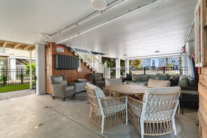 An outdoor covered patio area with wicker furniture, a round table, and a staircase leading to an upper level. - Private Pool and Hot Tub — 5BR/4BA Beach House with Ocean Views in Surfside Beac (Surfside Beach)