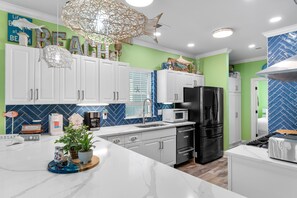 A modern kitchen with white cabinetry, a black refrigerator, and a blue and white tiled backsplash. - Private Pool and Hot Tub — 5BR/4BA Beach House with Ocean Views in Surfside Beac (Surfside Beach)