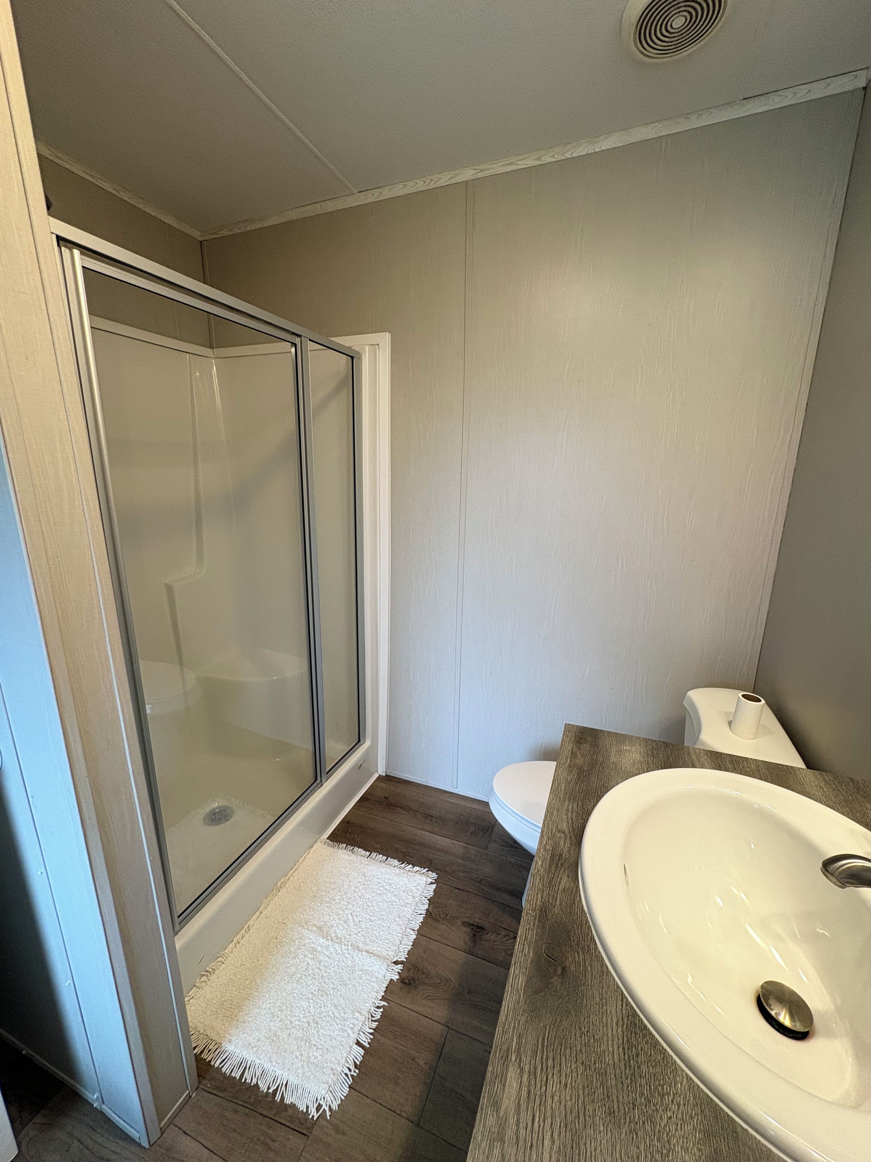 Une salle de bain avec une douche à parois de verre, des toilettes blanches et un meuble-lavabo en bois avec un évier.