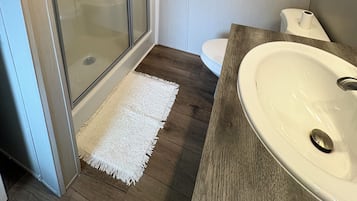 Une salle de bain avec une douche à parois de verre, des toilettes blanches et un meuble-lavabo en bois avec un évier.