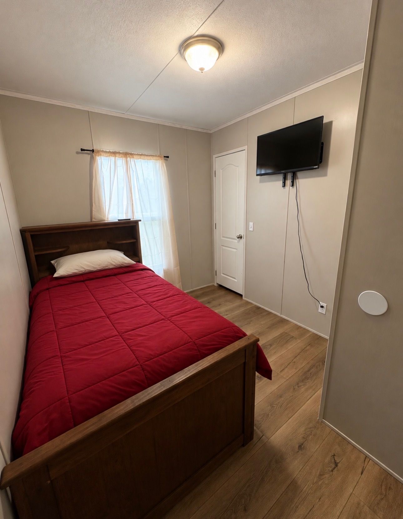 Un dormitorio con cama de madera, televisor montado en la pared y una puerta.