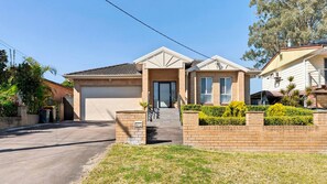 A residential house with a garage, a front porch, and a well-maintained lawn. - The Sanctuary House By Book Jervis Bay (Sanctuary Point)