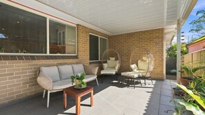 A covered patio area with a brick wall, a sofa, two chairs, and a small table. - The Sanctuary House By Book Jervis Bay (Sanctuary Point)