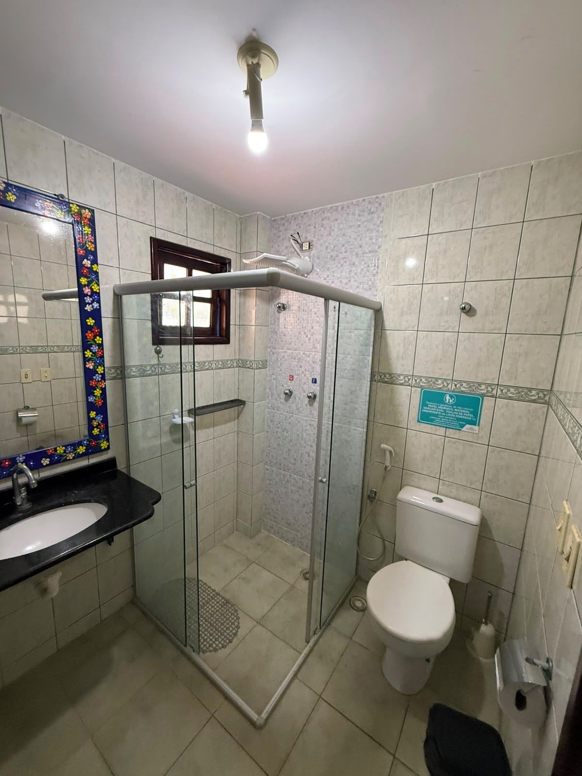 Une salle de bain dotée d’une douche à parois de verre, de toilettes blanches, d’un lavabo avec un plan de travail noir et d’un miroir orné d’un motif floral.