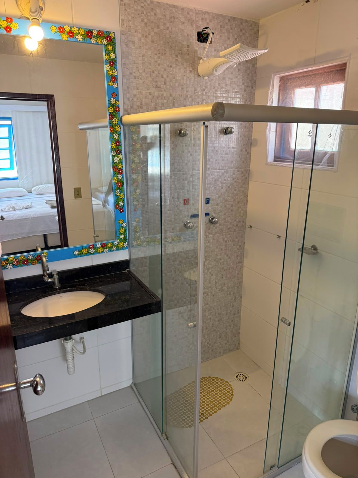 A bathroom with a glass-enclosed shower, a sink with a mirror, and a toilet.
