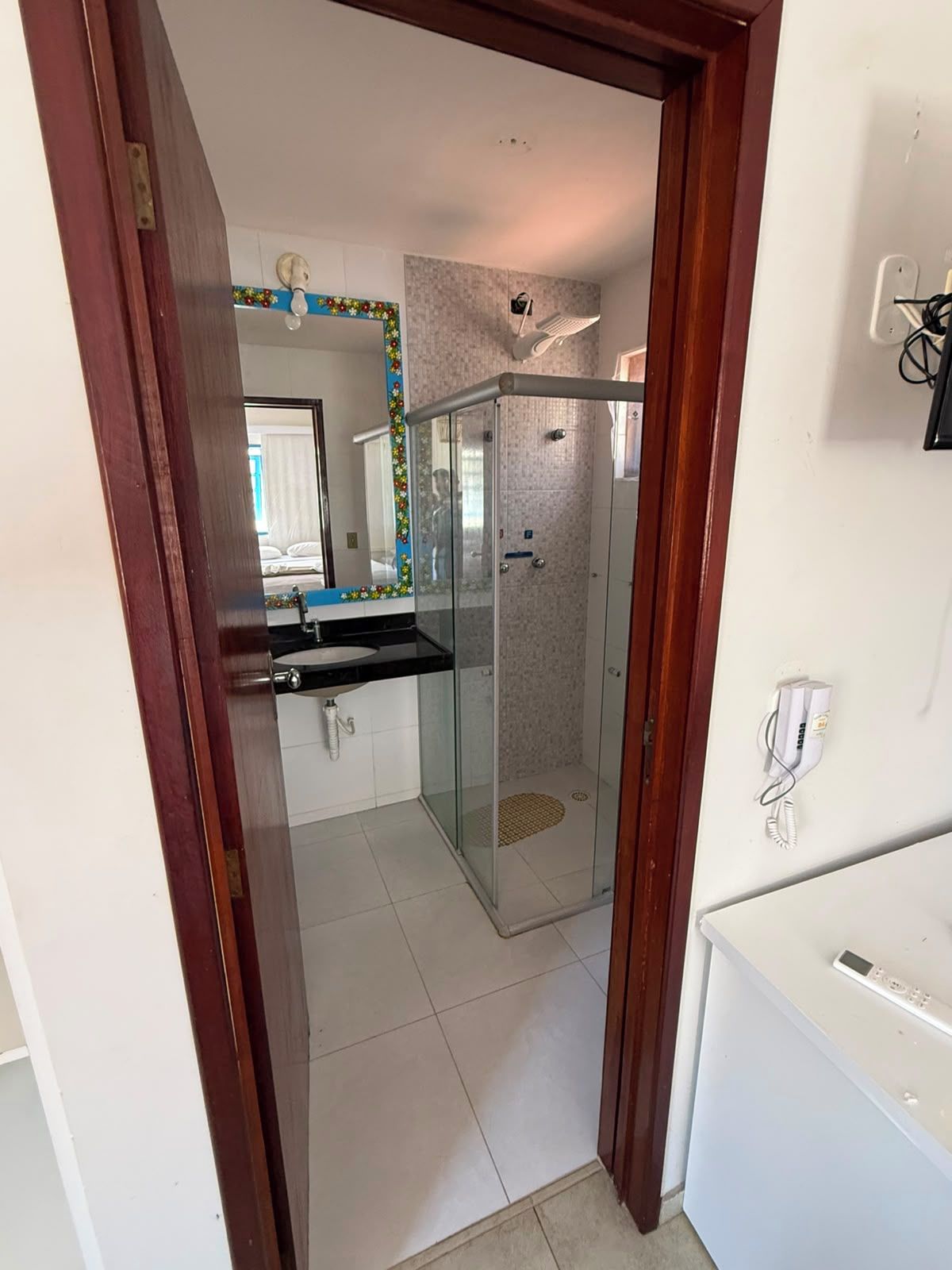 A bathroom with a glass-enclosed shower, a white sink, and a mirror with a decorative border.