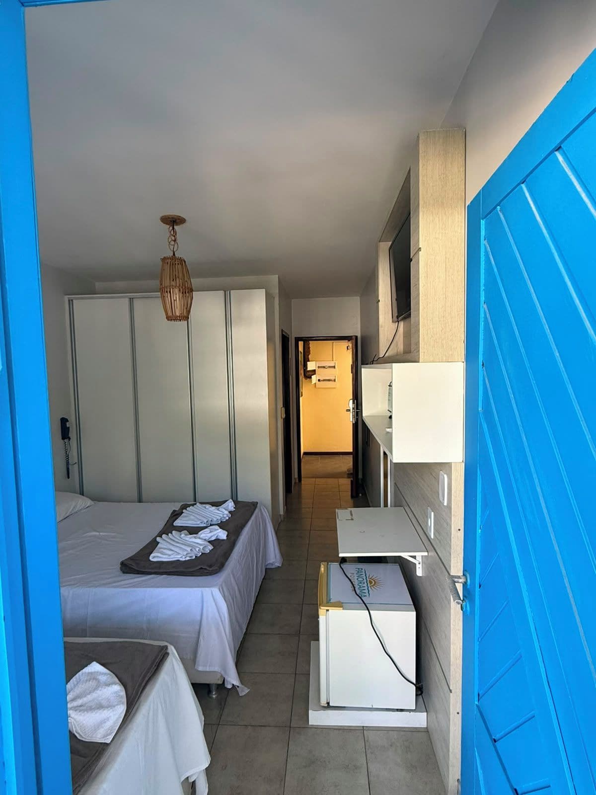 Une chambre d’hôtel avec un lit, une table de chevet, un petit bureau avec un ordinateur et une porte bleue.