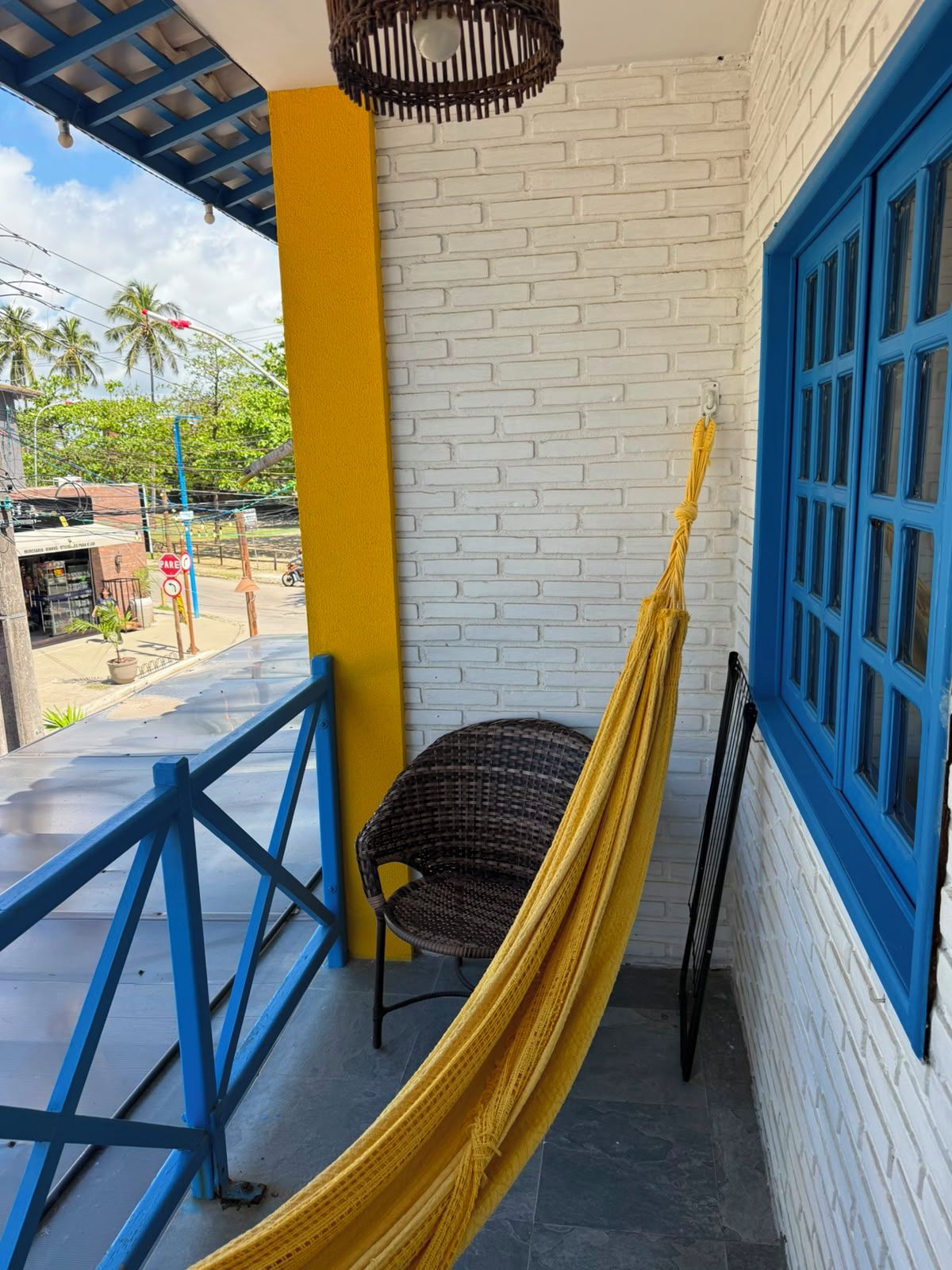 A hammock on a balcony with a white brick wall and blue-framed window.