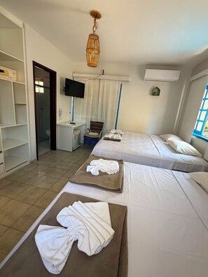 Habitación de hotel con dos camas, televisión, escritorio y baño visible a través de una puerta abierta.