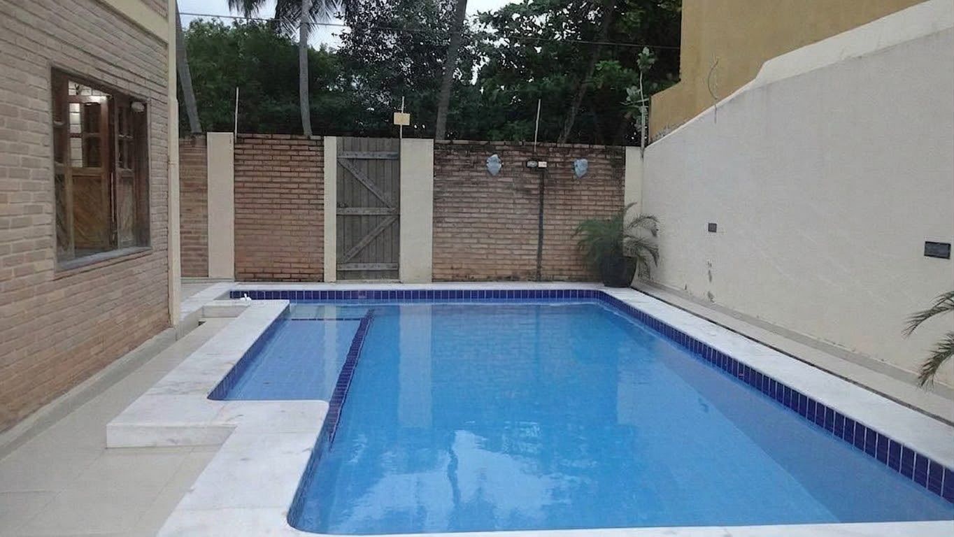 A rectangular swimming pool with a tiled edge, surrounded by a brick wall and a white wall.
