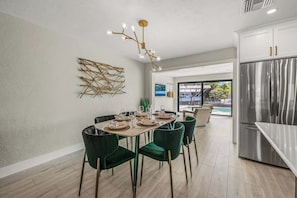 Eine moderne Küche mit einem Edelstahl-Kühlschrank, ein Essbereich mit Tisch für vier Personen und Blick auf einen Pool durch große Fenster.