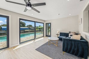 Ein modernes Wohnzimmer mit Blick auf einen Pool, einem Deckenventilator und einem dunkelblauen Sofa.