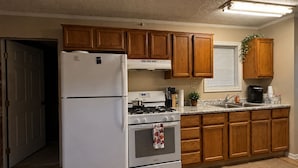 A kitchen with wooden cabinets, a white refrigerator, a stove, and a sink. - Ole Miss Football Game Rental! (Como)