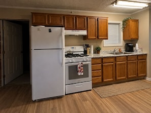 A kitchen with wooden cabinets, a white refrigerator, a stove, and a sink. - Ole Miss Football Game Rental! (Como)